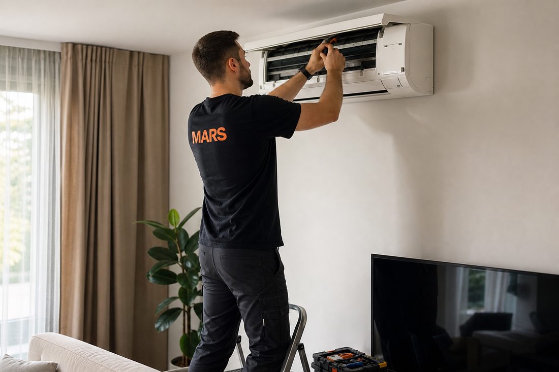 Technician in a black Mars t-shirt servicing a wall-mounted air conditioner